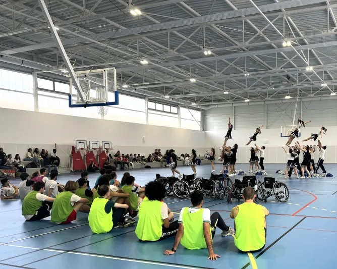 Personnes en dossard dans un gymnase regardant un spectacle de cheerleaders, des fauteuils roulants sont également disposés